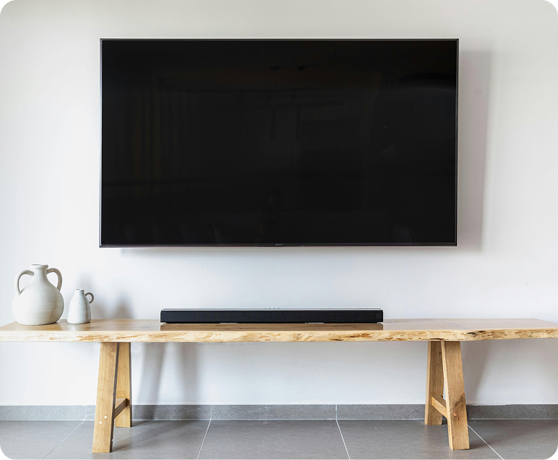 New television mounted on wall above a wooden table.