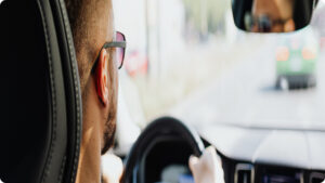 rideshare driver man wearing sunglasses driving a car in traffic, viewed from behind driver's seat