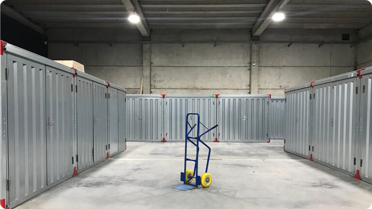 Interior of a self-storage facility with rows of metal storage units and a hand truck in the aisle
