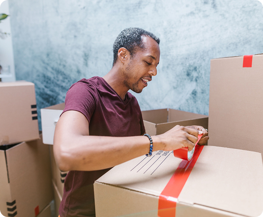 Man taping a cardboard moving box while sorting belongings during a decluttering project
