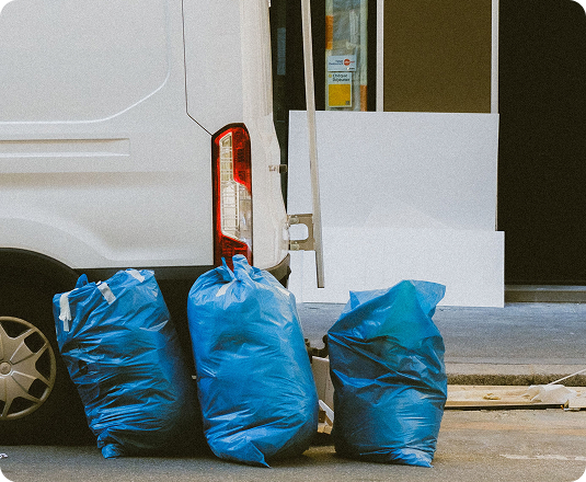 Blue trash bags and discarded items loaded next to a van during a storage unit cleanout