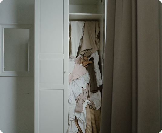 Cluttered closet with clothes and linens piled haphazardly before an organizing project